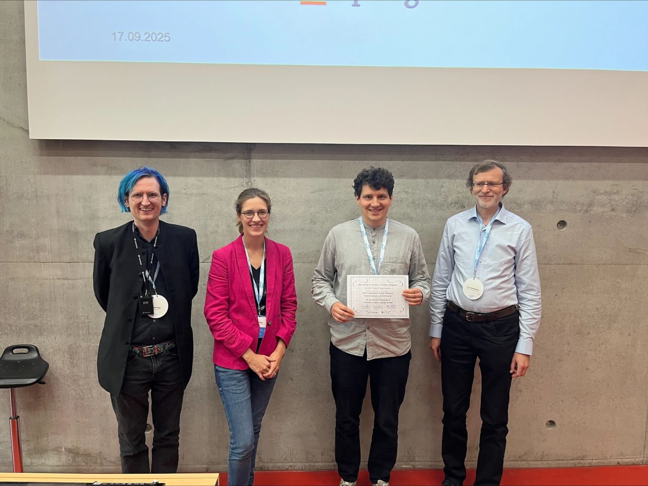 Mario Koddenbrock holding the KI 2025 Best Paper Award certificate at the award ceremony, next to three other conference participants