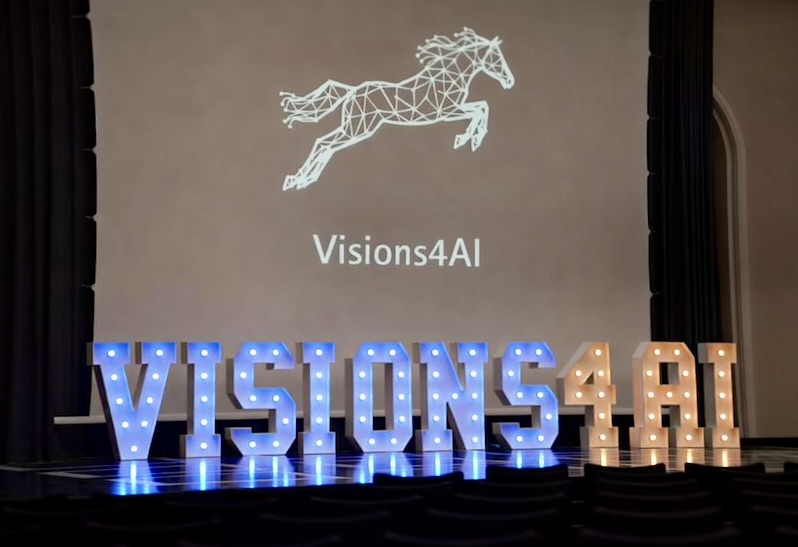 Illuminated Visions4AI letters on a stage, with the event logo projected behind them